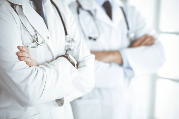 Een groep onbekende dokters staat als een team met gekruiste armen in het ziekenhuiskantoor, close-up. Medische hulp, verzekering in de gezondheidszorg en geneeskunde concept — Stockfoto