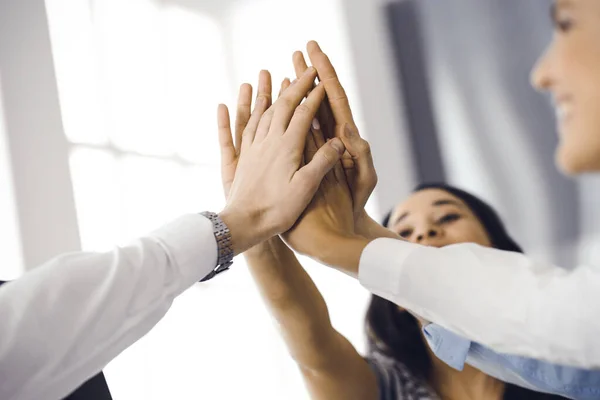 Group of business people joining hands or giving five to each other after meeting or negotiation in modern office. Colleagues showing teamwork, cooperation and partnership in corporate occupation