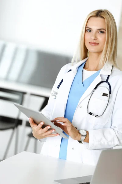 Mujer-médico en el trabajo en la clínica emocionada y feliz de su profesión. Mujer rubia médico está sonriendo mientras se utiliza la tableta. Concepto de medicina — Foto de Stock