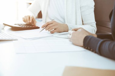 Mali durumu kontrol eden ya da vergi formları için hesap makinesinin geliri ile sayan, elleri yakın çekim. İş kadını ofisteki masada iş arkadaşıyla oturuyor ve çalışıyor. Vergi ve Denetim kavramı