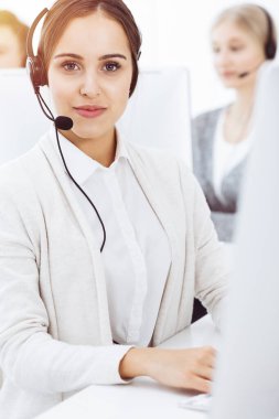 Güneşli ofiste çağrı merkezi. Çeşitli operatörler iş başında. Telepazarlama servisinin müşterileriyle iletişim kuran kulaklıklı güzel bir kadın.