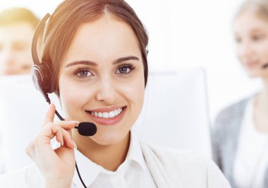 Güneşli ofiste çağrı merkezi. Çeşitli operatörler iş başında. Telepazarlama servisinin müşterileriyle iletişim kuran kulaklıklı güzel bir kadın.