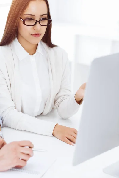 Mujer joven sentada en el escritorio con computadora en la oficina de color blanco. Parece estudiante o dama de negocios comunicándose con el hombre vestido casual — Foto de Stock