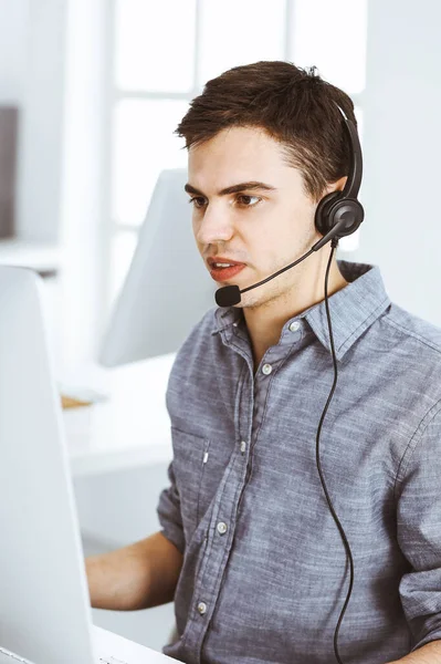 Nenuceně oblečený mladý muž pomocí sluchátka a počítače při rozhovoru se zákazníky on-line. Call centrum, obchodní koncept — Stock fotografie