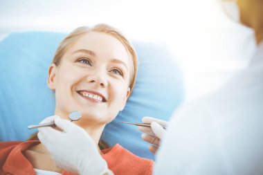 Mutlu kadın dişçi kliniğinde dişçi tarafından muayene ediliyor. Sağlıklı dişler ve ilaçlar, stomatoloji konsepti