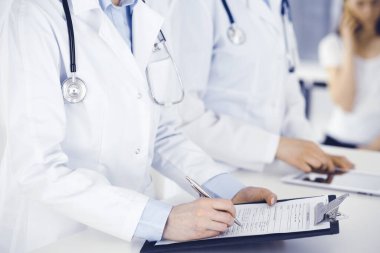 İş yerindeki bilinmeyen kadın doktorlar, arka planda hastaları var. Hastane resepsiyonunda beklerken tıbbi belgeleri dolduran kadın doktorlar, yakın plan. Sağlık hizmeti kavramı