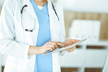 Bilinmeyen kadın doktor klinikte duruyor ve tablet bilgisayar kullanıyor, yakın plan. Veriler ve tıp ve sağlık hizmetlerindeki en iyi hizmet