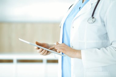 Bilinmeyen kadın doktor klinikte duruyor ve tablet bilgisayar kullanıyor, yakın plan. Tıp ve sağlık alanlarındaki veriler
