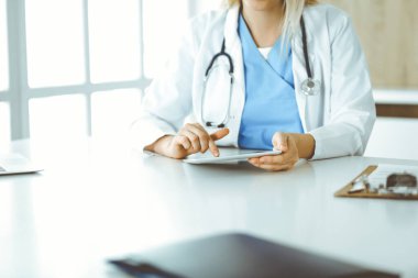 Bilinmeyen kadın doktor klinikte duruyor ve tablet bilgisayar kullanıyor, yakın plan. Veriler ve tıp ve sağlık hizmetlerindeki en iyi hizmet