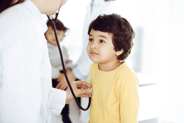 Egy nő-orvos sztetoszkóppal vizsgál meg egy gyermekbeteget. Aranyos arab fiú az orvosnál. Orvosi segítség koncepció — Stock Fotó