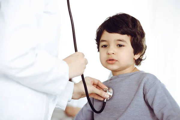 Médico-mujer examinando a un niño paciente por estetoscopio. Lindo chico árabe y su hermano en la cita con el médico. Concepto de medicina —  Fotos de Stock