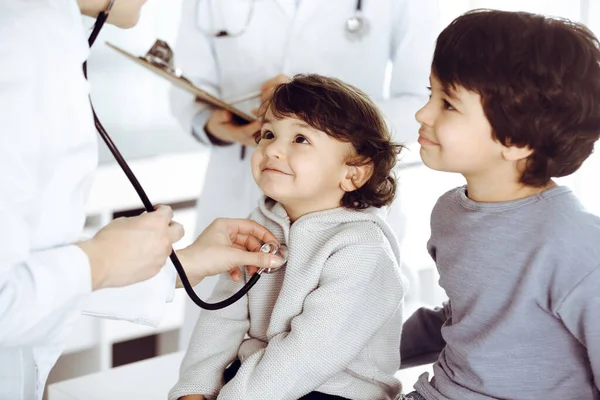 Женщина-врач осматривает ребенка стетоскопом. Милый арабский малыш и его брат на приеме у врача. Концепция медицины — стоковое фото
