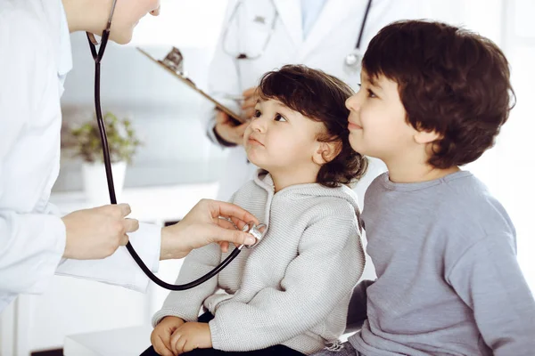 Egy nő-orvos sztetoszkóppal vizsgál meg egy gyermekbeteget. Aranyos arab kisbaba és a bátyja az orvosi vizsgálaton. Orvosi fogalom — Stock Fotó