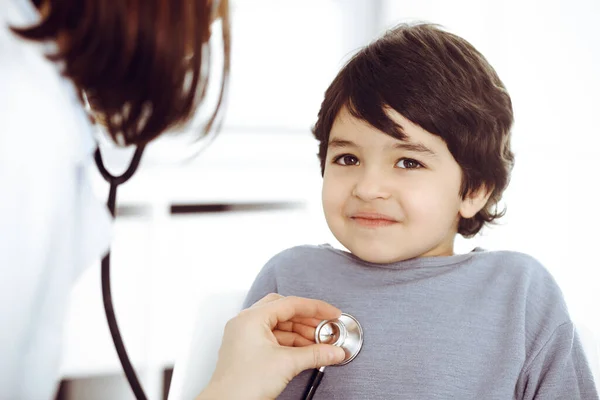 Médico-mujer examinando a un niño paciente por estetoscopio. Lindo chico árabe en la cita con el médico. Concepto de medicina —  Fotos de Stock