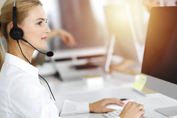 Blond affärskvinna använder headset för kommunikation och konsultera folk på soligt kontor. Anropscentral — Stockfoto