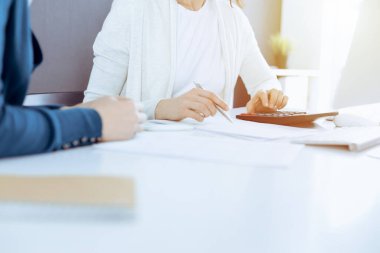 Mali durumu kontrol eden ya da vergi formları için hesap makinesinin geliri ile sayan, elleri yakın çekim. İş kadını ofisteki masada iş arkadaşıyla oturuyor ve çalışıyor. Vergi ve Denetim kavramı