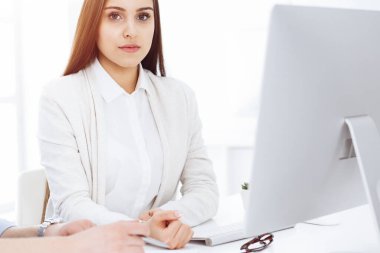 Genç, neşeli bir kadın bilgisayarla masada oturuyor ve güneşli ofisteki kameraya bakıyor. Öğrenci kız ya da iş kadını gibi görünüyor.