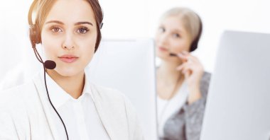 Güneşli ofiste çağrı merkezi. Çeşitli operatörler iş başında. Telepazarlama servisinin müşterileriyle iletişim kuran kulaklıklı güzel bir kadın.