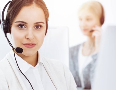 Güneşli ofiste çağrı merkezi. Çeşitli operatörler iş başında. Telepazarlama servisinin müşterileriyle iletişim kuran kulaklıklı güzel bir kadın.