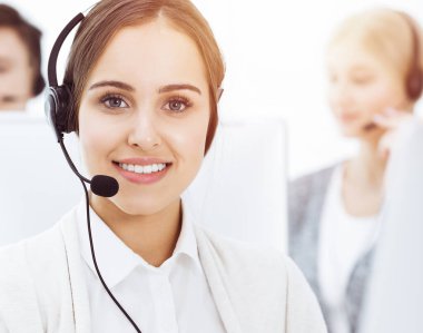 Güneşli ofiste çağrı merkezi. Çeşitli operatörler iş başında. Telepazarlama servisinin müşterileriyle iletişim kuran kulaklıklı güzel bir kadın.