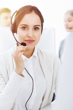 Güneşli ofiste çağrı merkezi. Çeşitli operatörler iş başında. Telepazarlama servisinin müşterileriyle iletişim kuran kulaklıklı güzel bir kadın.
