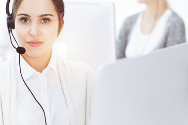 Güneşli ofiste çağrı merkezi. Çeşitli operatörler iş başında. Telepazarlama servisinin müşterileriyle iletişim kuran kulaklıklı güzel bir kadın.
