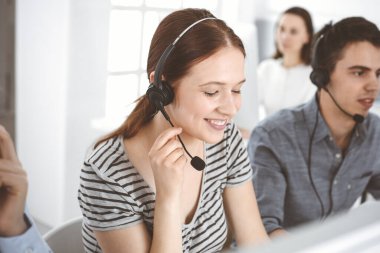 İnternette müşterilerle konuşurken kulaklık ve bilgisayar kullanan sıradan giyinmiş genç bir kadın. Bir grup operatör iş başında. Çağrı merkezi, iş konsepti