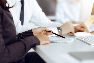 İş kadını ve erkek, güneşli ofiste bilgisayar ve bloknot kullanırken soruları tartışıyorlar.