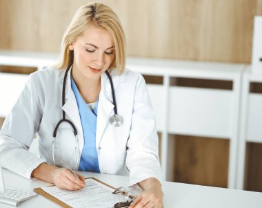 Hastanedeki ya da klinikteki masa başında oturan kadın doktor. Sarışın, neşeli doktor ilaç geçmişi formunu dolduruyor.