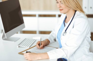 Hastanedeki ya da klinikteki masa başında oturan kadın doktor. Sarışın, neşeli doktor ilaç geçmişi formunu dolduruyor.