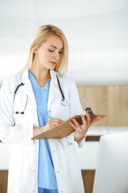 Kadın doktor hastanede ya da klinikte duruyor ve ilaç geçmişi formunu dolduruyor. Veriler ve tıp ve sağlık hizmetlerindeki en iyi hizmet