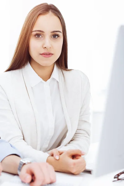 Tânăra femeie veselă stând la birou cu calculatorul și uitându-se la camera foto în biroul însorit. Arată ca o studentă sau o femeie de afaceri — Fotografie, imagine de stoc