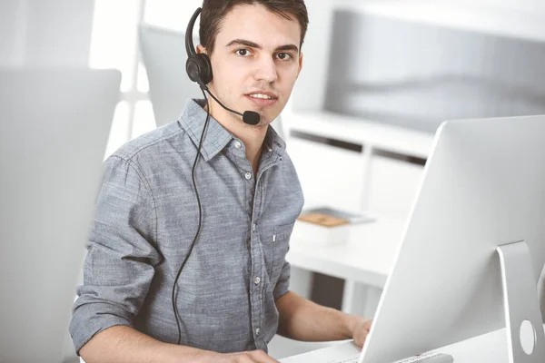 Hombre joven vestido casual usando auriculares y computadora mientras habla con los clientes en línea. Call center, concepto de negocio —  Fotos de Stock