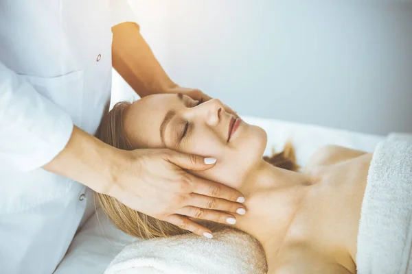 Gelukkige vrouw genieten van gezichtsmassage met gesloten ogen in spa salon. Ontspannende behandeling in de geneeskunde en Beauty concept — Stockfoto