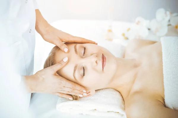 Mooie blanke vrouw geniet van gezichtsmassage met gesloten ogen in spa salon. Ontspannende behandeling in de geneeskunde en Beauty concept — Stockfoto