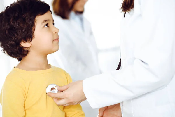 Mujer-médico examinando a un niño paciente por estetoscopio. Lindo chico árabe en la cita con el médico. Medicina ayuda concepto —  Fotos de Stock
