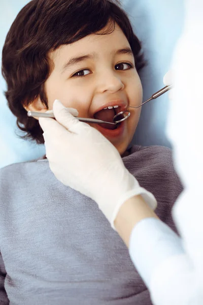 Pequeño chico árabe sentado en la silla dental con la boca abierta durante la revisión oral con el médico dentista. Concepto de estomatología — Foto de Stock