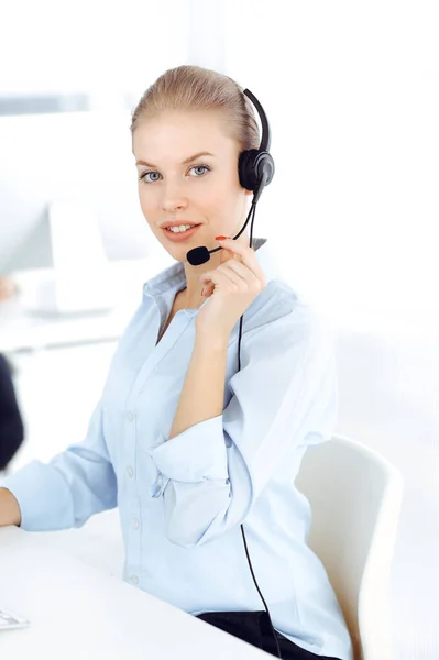 Mujer rubia operador de llamadas está utilizando la computadora y auriculares para consultar a los clientes en línea. Grupo de personas diversas que trabajan como ocupación de servicio al cliente. Concepto empresarial —  Fotos de Stock