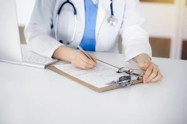Mulher-médico desconhecido no trabalho preenchendo formulário de registro de histórico de medicação na clínica ensolarada, close-up — Fotografia de Stock