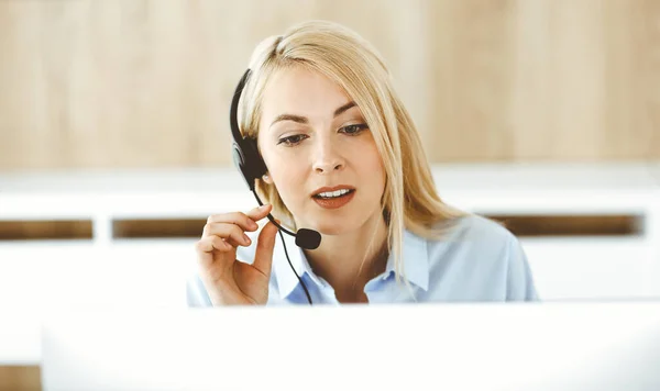 Donna d'affari bionda seduta e comunicata da auricolare in ufficio call center. Concetto di attività di televendita o professione di home office — Foto Stock