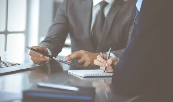 Uomo d'affari sconosciuto che utilizza tablet e lavora insieme al suo collega mentre si siede alla scrivania di vetro in un ufficio moderno. Concetto di lavoro di squadra e partenariato — Foto Stock