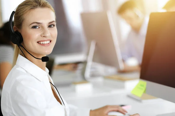 Blond affärskvinna använder headset för kommunikation och konsultera folk på soligt kontor. Anropscentral — Stockfoto