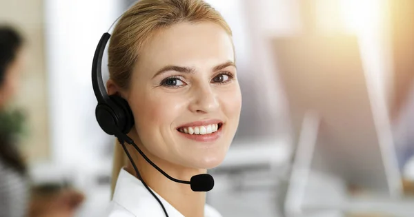 Blonďatá obchodnice používající sluchátka pro komunikaci a poradu s lidmi ve slunné kanceláři. Centrum volání — Stock fotografie