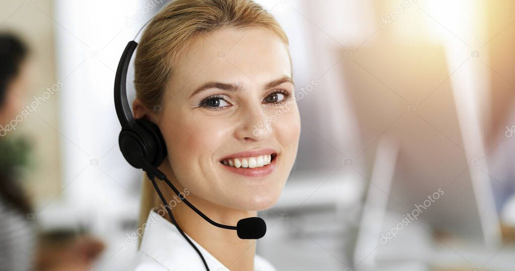 Blond business woman using headset for communication and consulting people at sunny office. Call center