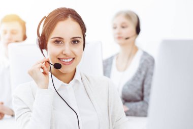 Güneşli ofiste çağrı merkezi. Çeşitli operatörler iş başında. Telepazarlama servisinin müşterileriyle iletişim kuran kulaklıklı güzel bir kadın.
