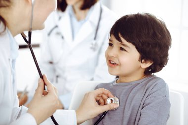 Doktor-kadın bir çocuğu steteskopla muayene ediyor. Doktor randevusunda tatlı bir Arap çocuk. Tıp konsepti