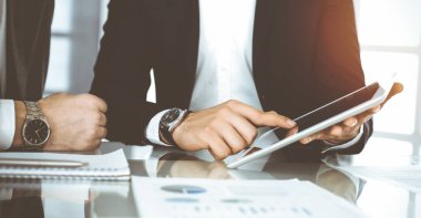 İş adamları güneşli ofiste çalışırken tablet bilgisayar kullanıyorlar. Bilinmeyen bir işadamı ortağıyla masada oturuyor.