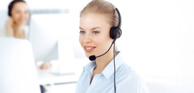 Sarışın kadın çağrı operatörü müşterilere danışmak için bilgisayar ve kulaklık kullanıyor. Müşteri hizmetleri işgali olarak çalışan bir grup insan. İş konsepti