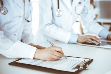 İş yerindeki bilinmeyen kadın doktorlar, arka planda hastaları var. Hastane resepsiyonunda beklerken tıbbi belgeleri dolduran kadın doktorlar, yakın plan. Sağlık hizmeti kavramı