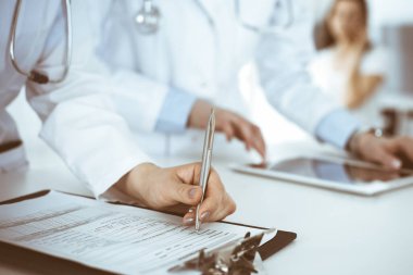 İş yerindeki bilinmeyen kadın doktorlar, arka planda hastaları var. Hastane resepsiyonunda beklerken tıbbi belgeleri dolduran kadın doktorlar, yakın plan. Sağlık hizmeti kavramı